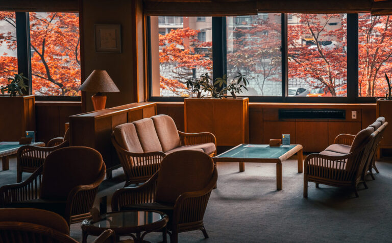 Lobby area of the Ryokan Daiichi Takimotokan featuring comfortable chairs and beige couches with red maple leaves outside the window